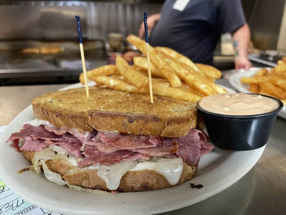 Reuben on grilled rye stacked with corned beef, sauerkraut and melted Swiss, with fries and a cup of 62 sauce